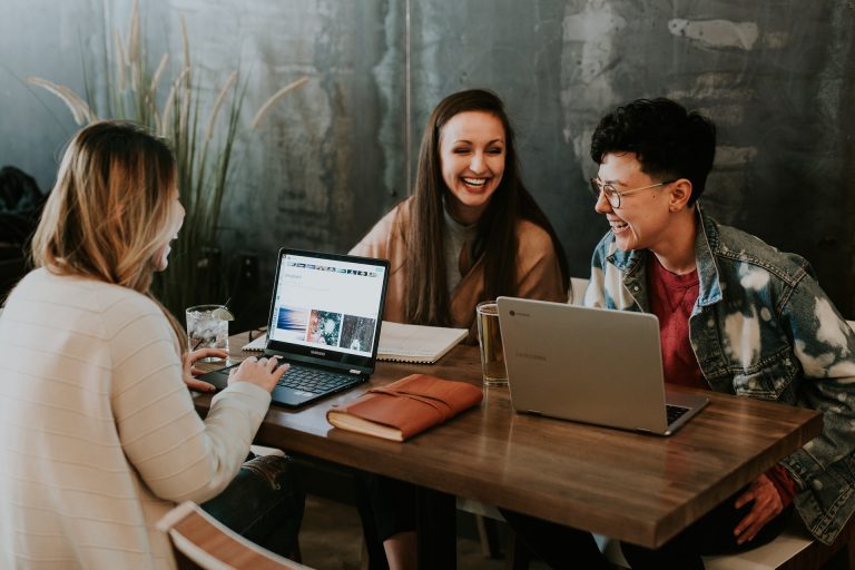 Três jovens sorrindo em mesa com seus computadores