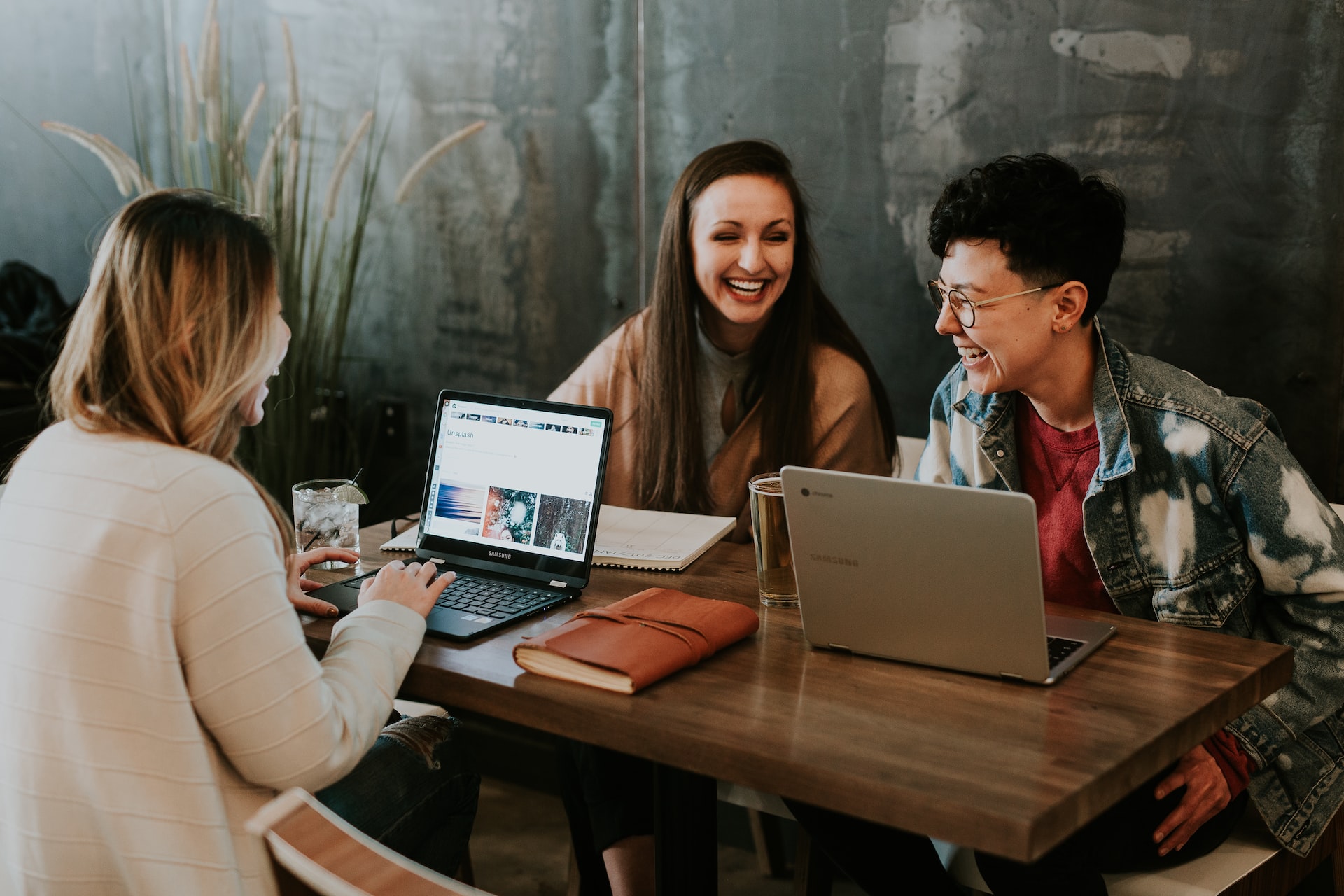 Três jovens sorrindo em mesa com seus computadores